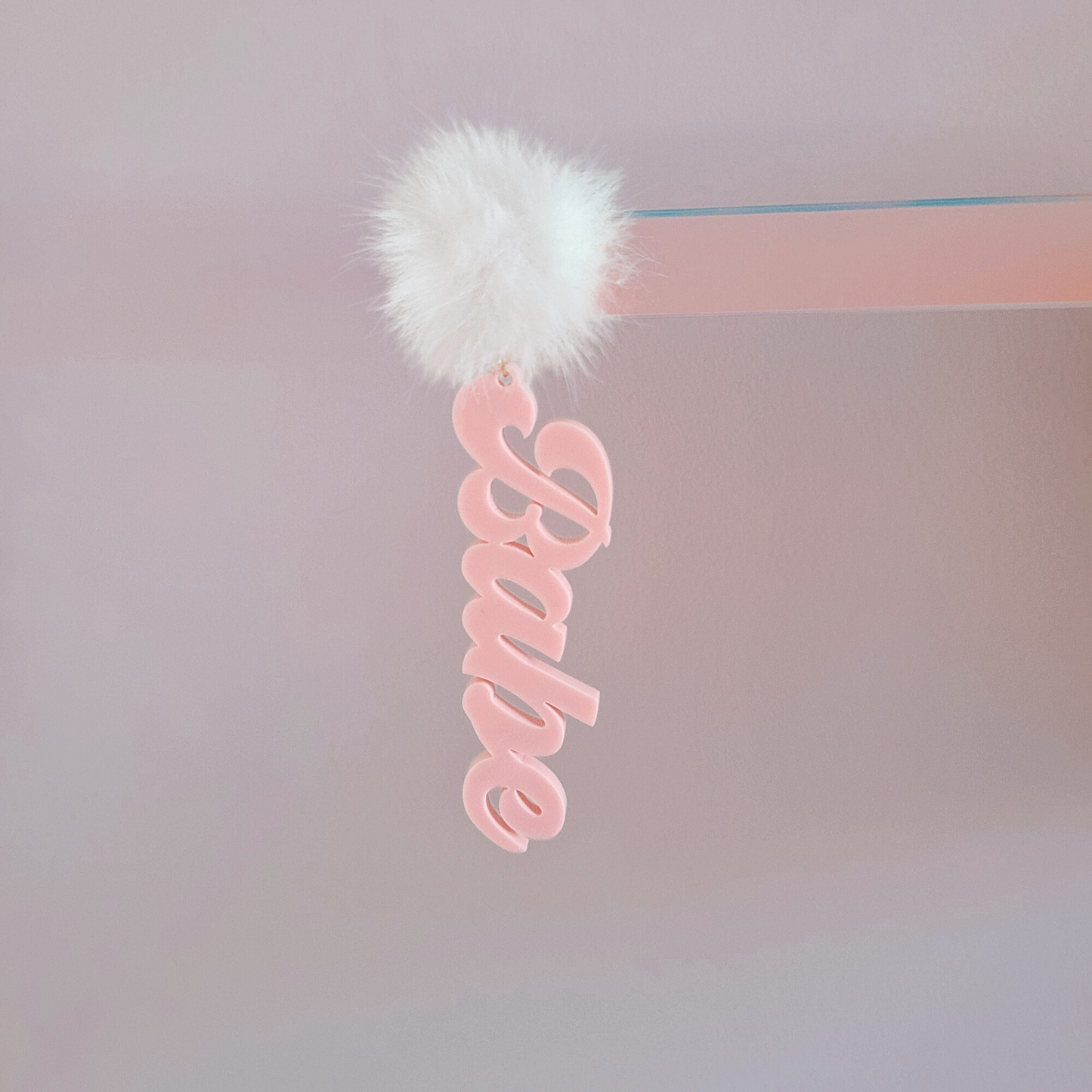 Pink 'Babe' earring with a white fluffy pom-pom on a white background
