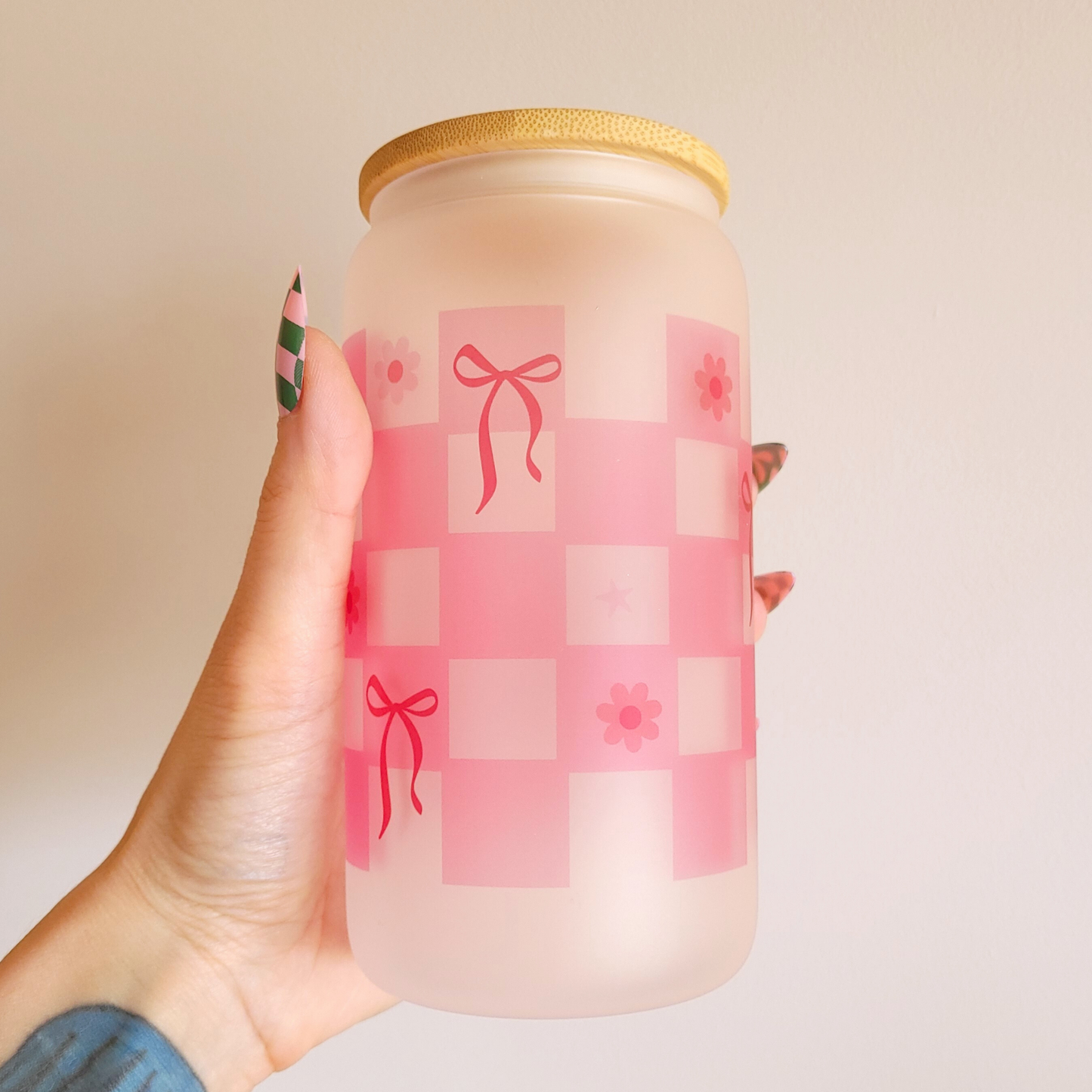 Frosted glass tumbler with pink checkered design, bows, and flowers held by hand