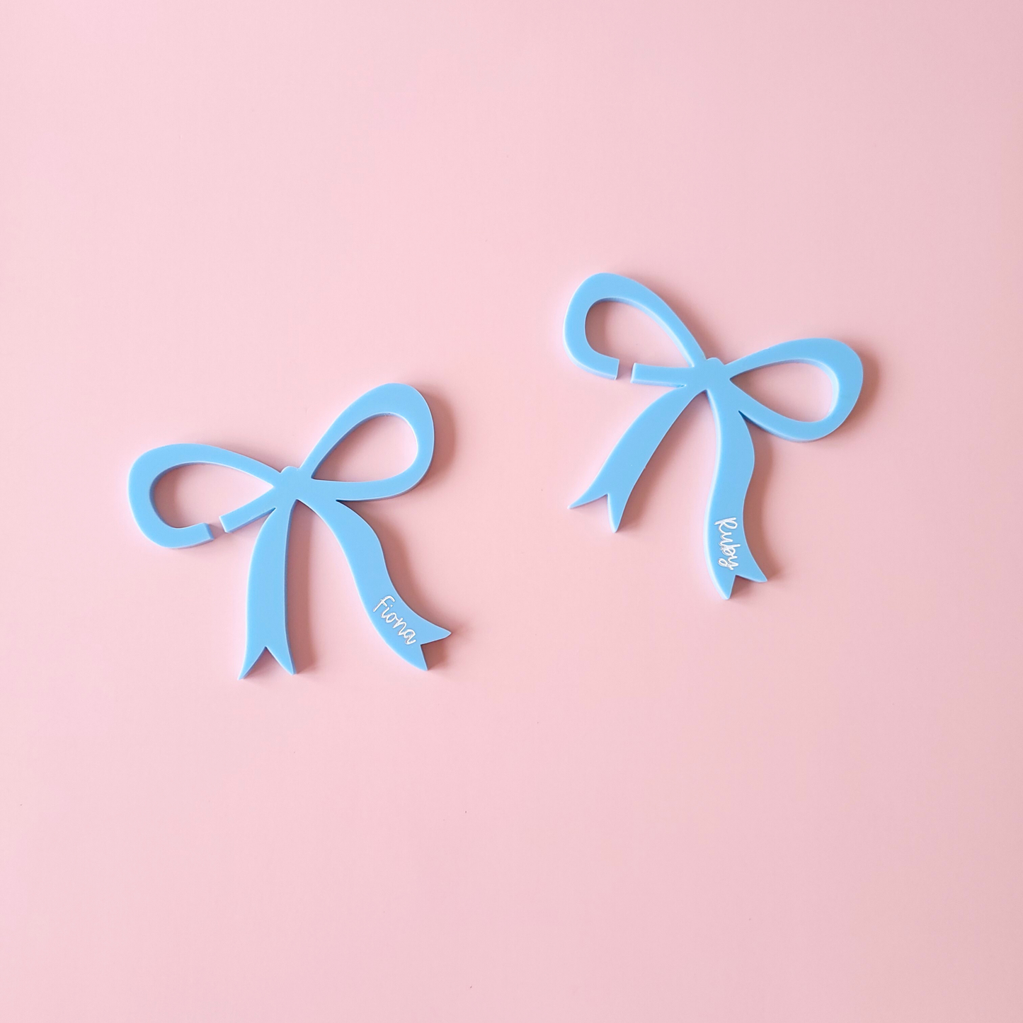 Blue acrylic bow drink charms with personalised names Fiona and Ruby on pastel background
