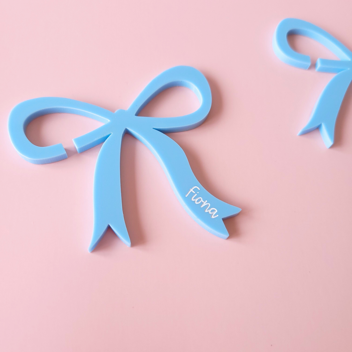 Close up of a pastel blue acrylic bow drink charms with personalised names on pastel background