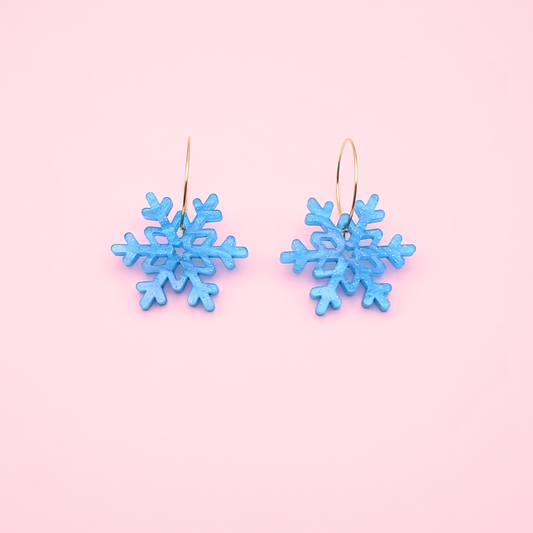 Blue glitter acrylic snowflake earrings on gold hoops — handmade winter dangle jewellery.