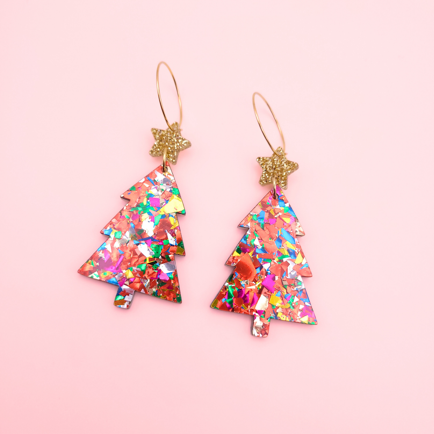 Rainbow acrylic Christmas tree earrings with gold glitter star toppers on a pink background.