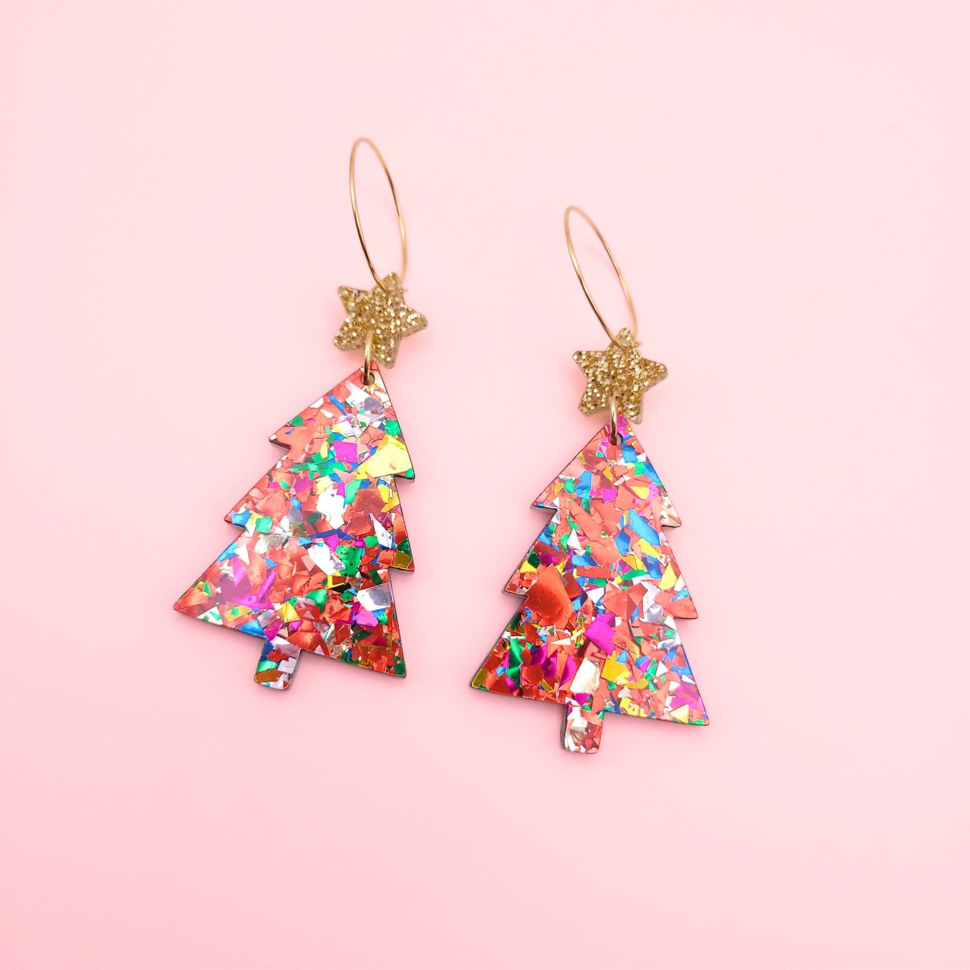 Rainbow acrylic Christmas tree earrings with gold glitter star toppers on a pink background.