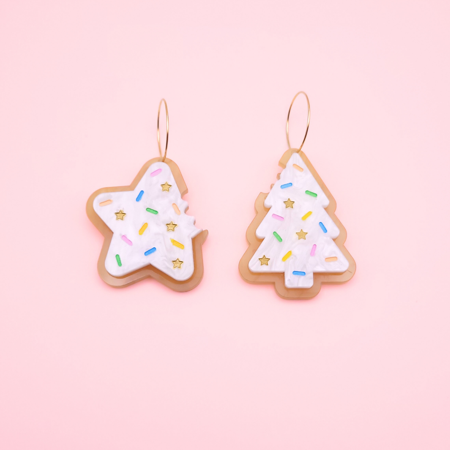 Christmas sugar cookie earrings shaped as a star and a tree with white frosting, pastel sprinkles, and gold star accents.