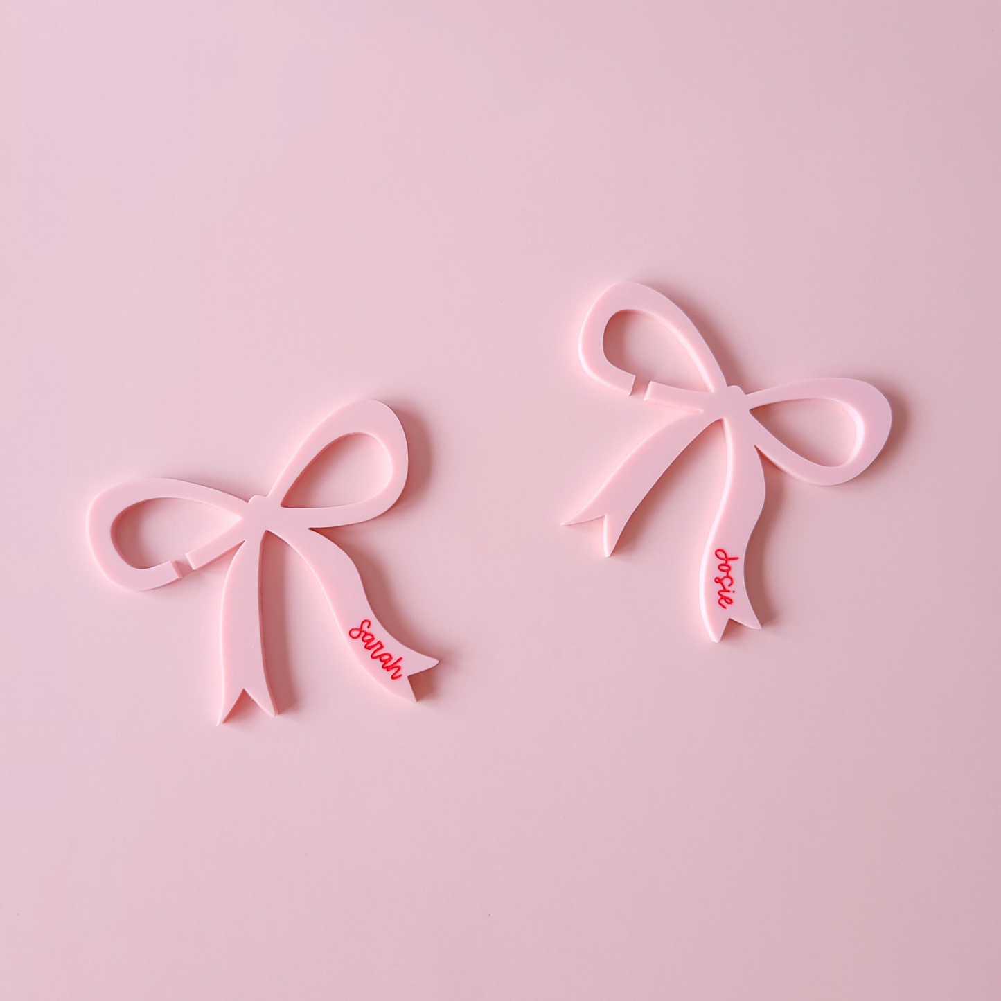 Pink acrylic bow drink charms with personalised names Sarah and Josie on pastel background
