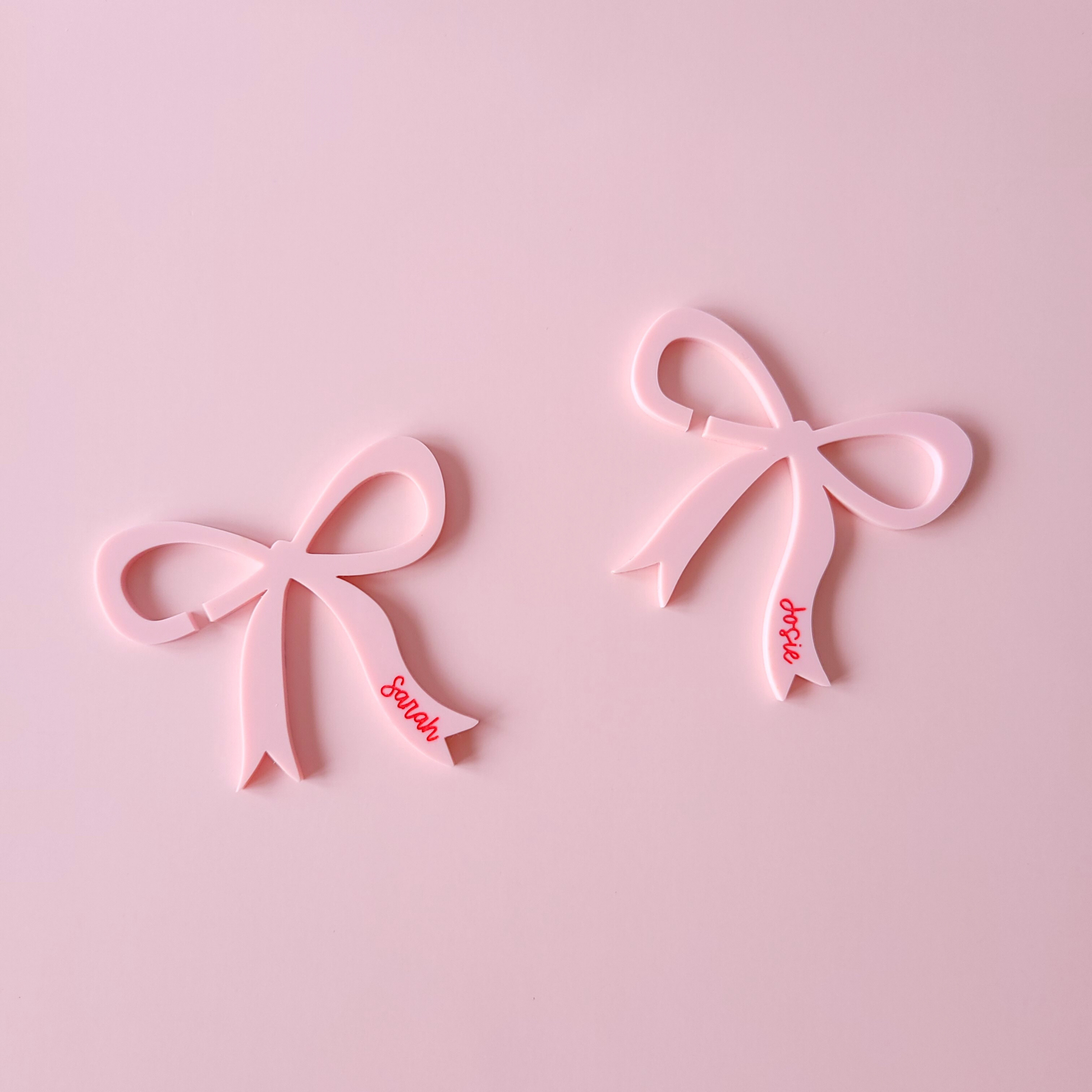 Pink acrylic bow drink charms with personalised names Sarah and Josie on pastel background
