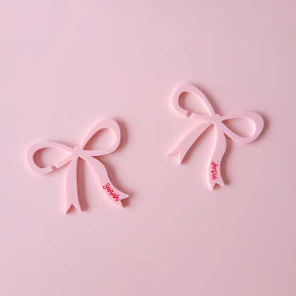 Pink acrylic bow drink charms with personalised names Sarah and Josie on pastel background