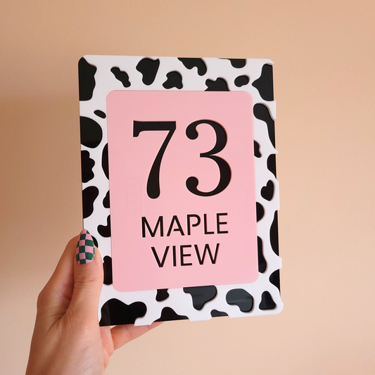 Pink acrylic house sign with bold black number 73 and Maple View text, framed by cow print border