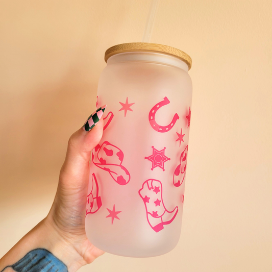 Western-themed frosted glass tumbler with pink cowgirl boots, hats, and stars design, bamboo lid and straw held by a hand