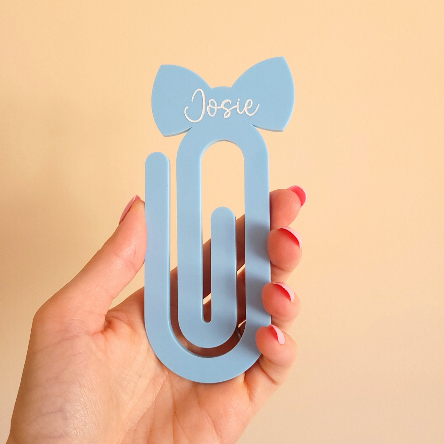Blue acrylic bow bookmark with custom name Josie in white text held by a hand