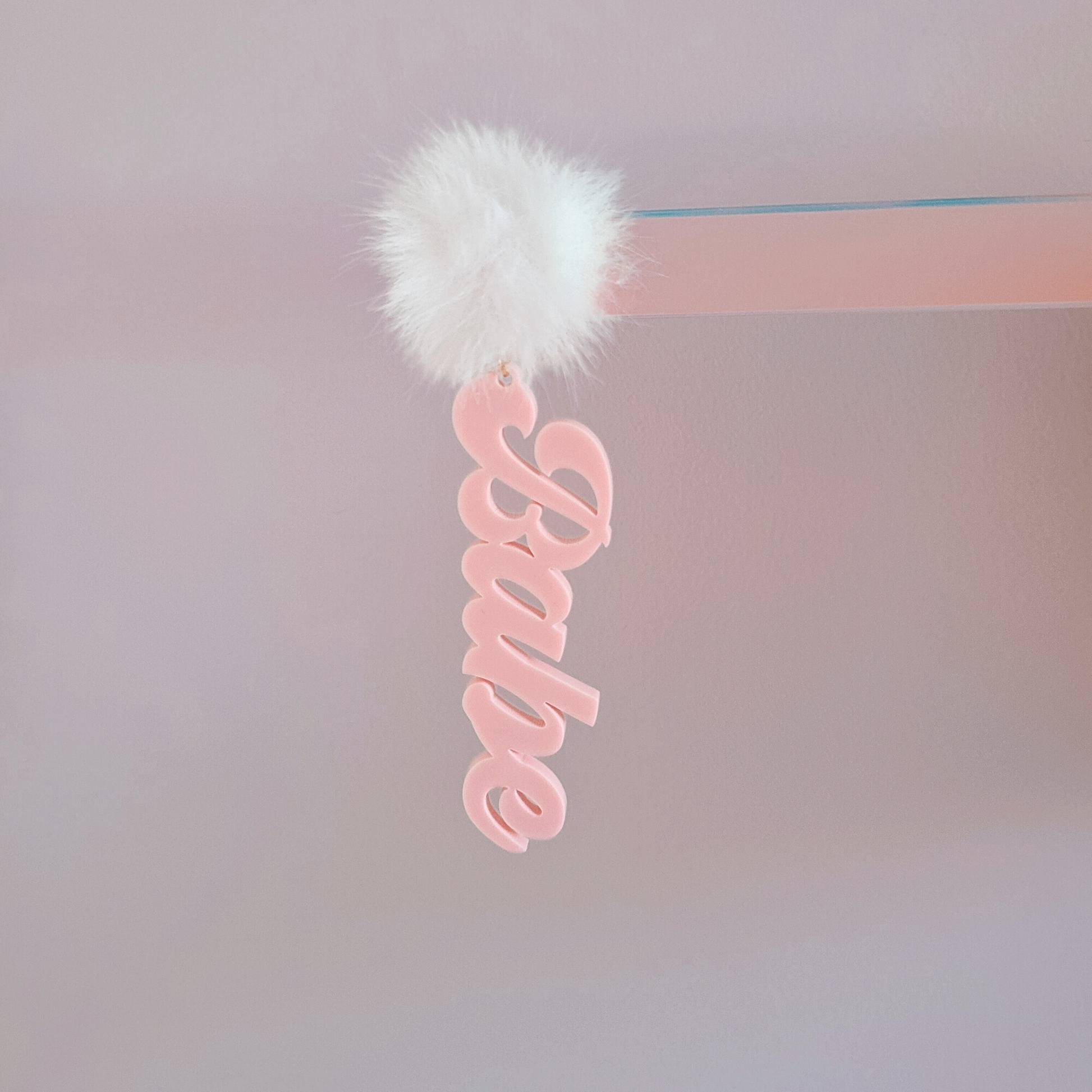 Pink 'Babe' earring with a white fluffy pom-pom on a white background