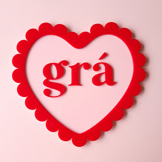 Heart-shaped frame with scalloped edges containing the word 'grá' on a pink background