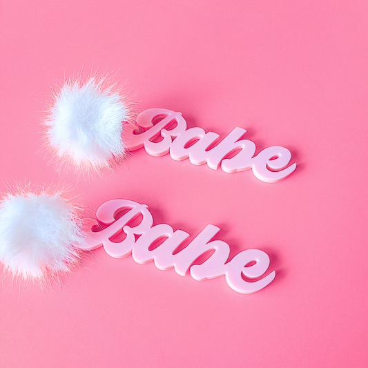 Pink 'Babe' earrings with white fluffy accents on a pink background