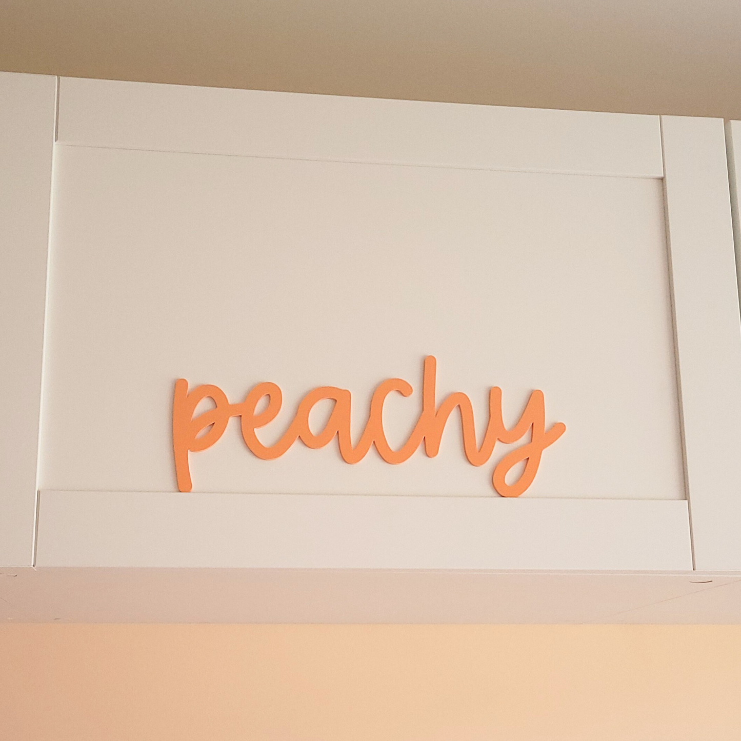 Modern acrylic script sign spelling peachy in soft pastel tones