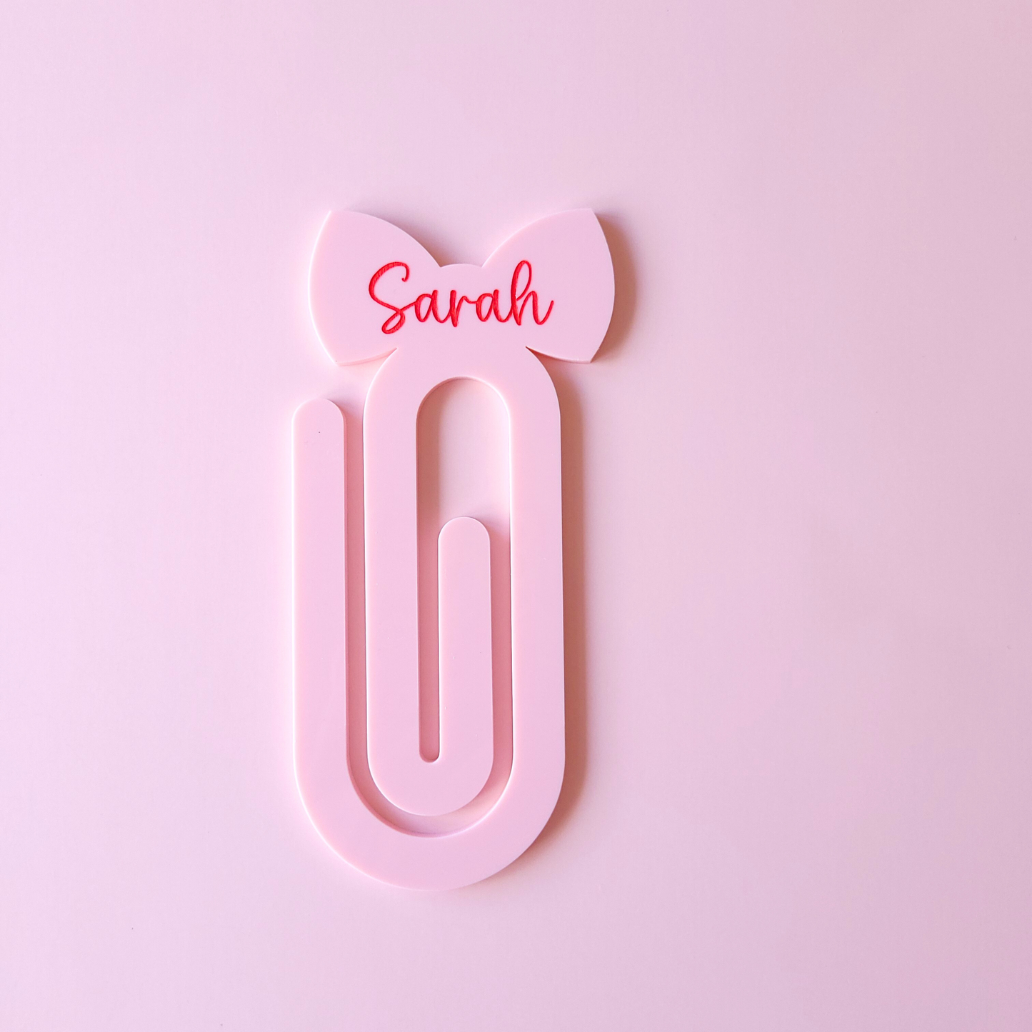 Pink acrylic bow bookmark with custom name Sarah in red text on pastel background