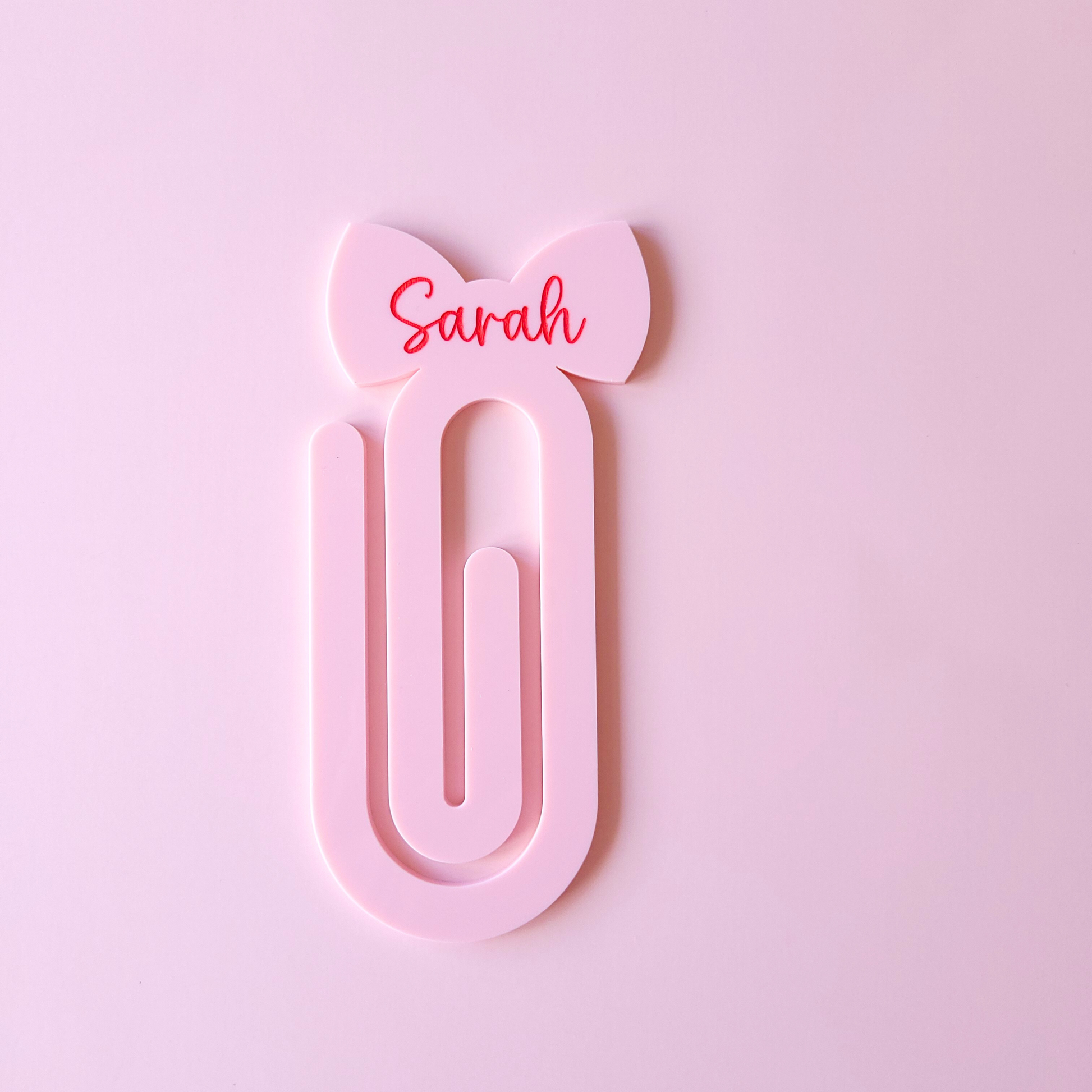 Pink acrylic bow bookmark with custom name Sarah in red text on pastel background