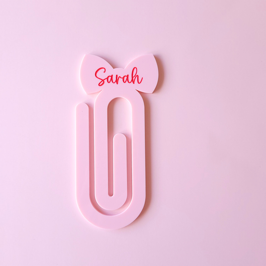 Pink acrylic bow bookmark with custom name Sarah in red text on pastel background