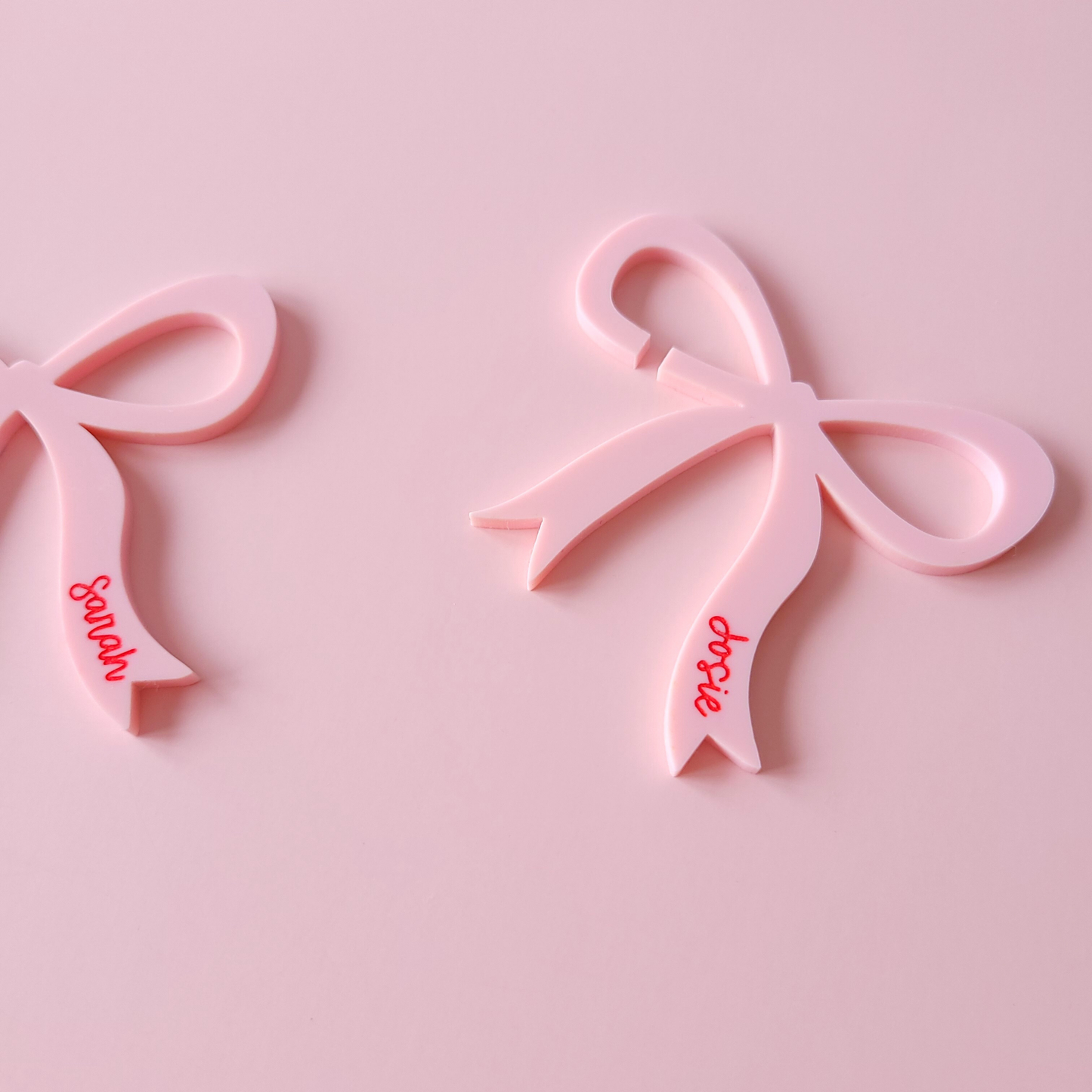 Pink acrylic bow drink charms with names Sarah and Josie on pastel background