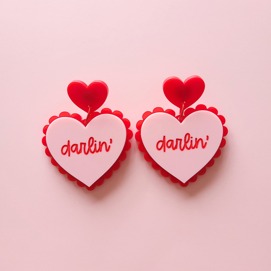 Heart-shaped earrings with 'darlin' text on a pink background