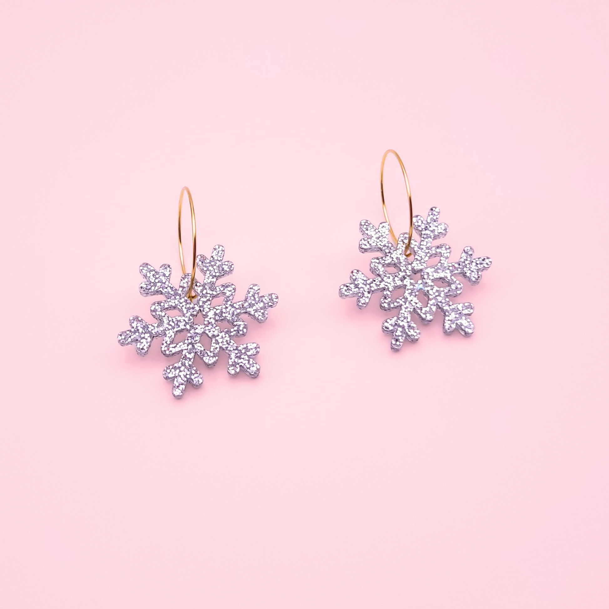 Silver glitter acrylic snowflake earrings on gold hoops — handmade festive winter dangle earrings.