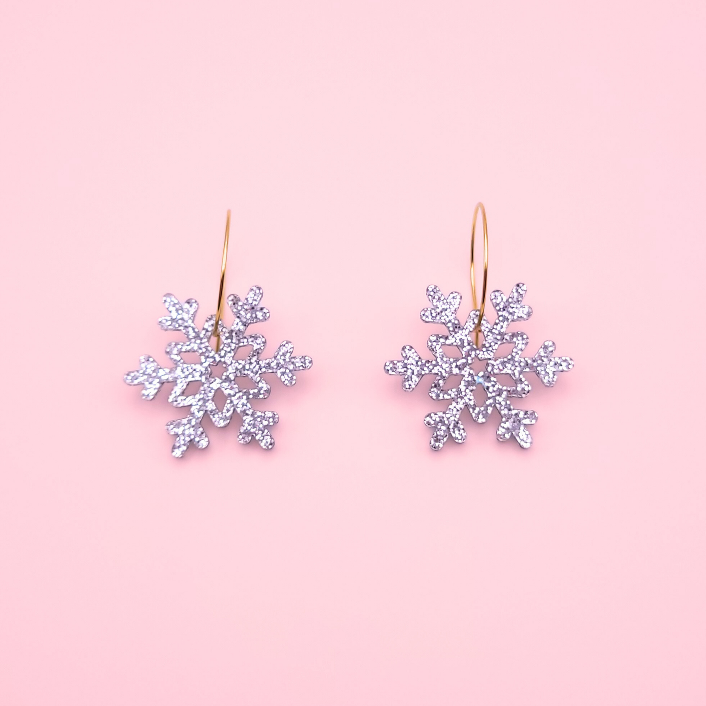 Silver glitter acrylic snowflake earrings on gold hoops — handmade festive winter dangle earrings.