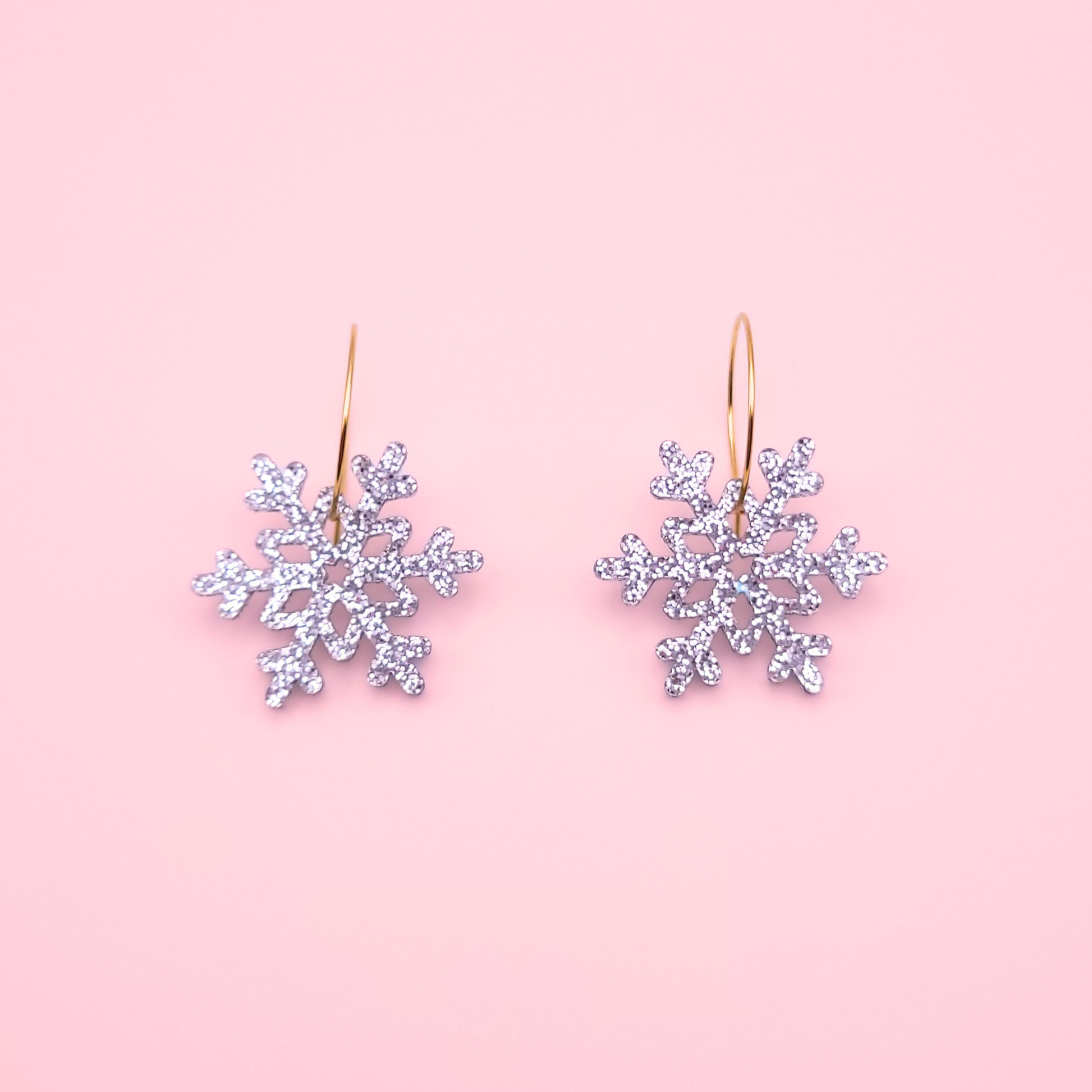 Silver glitter acrylic snowflake earrings on gold hoops — handmade festive winter dangle earrings.