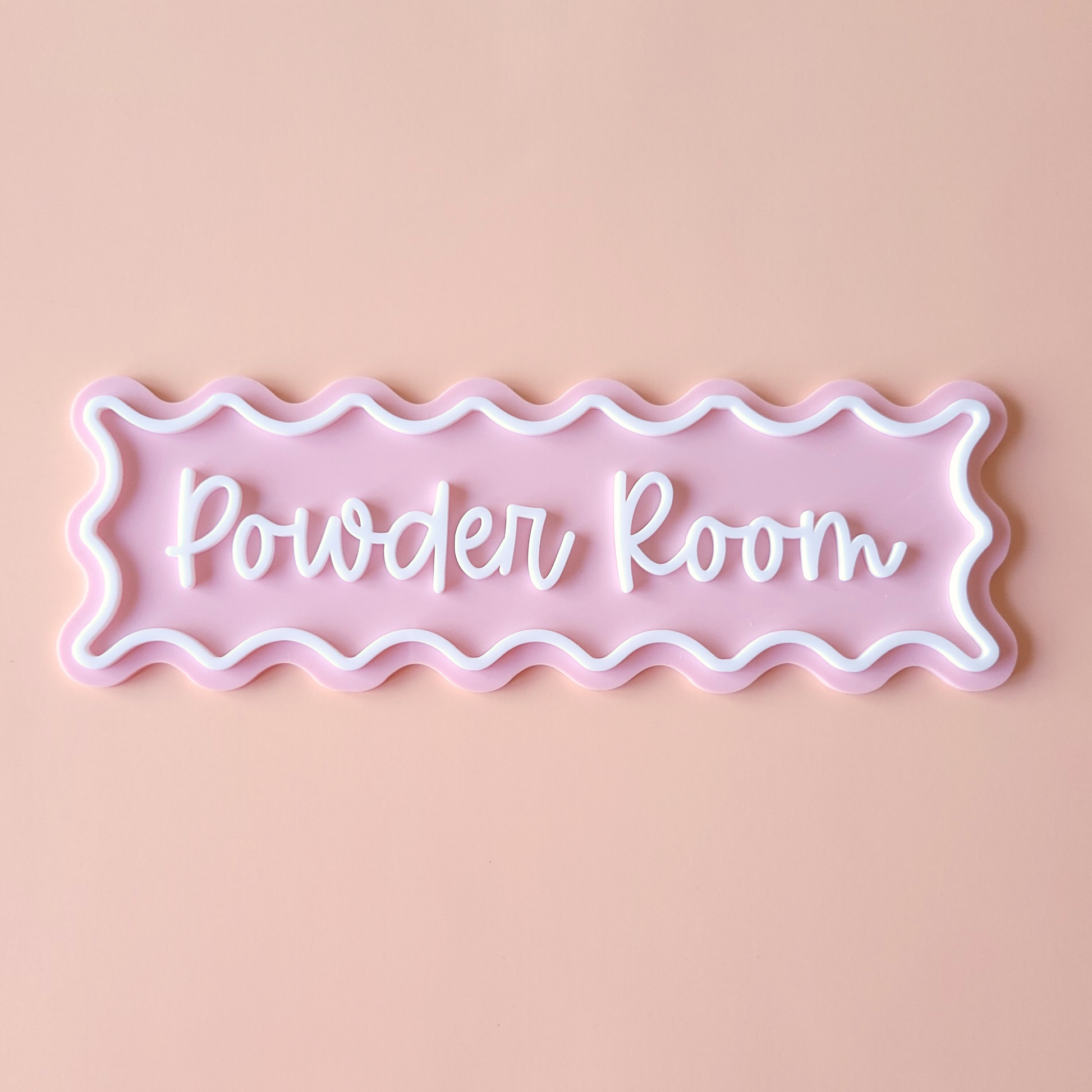 Pink acrylic Powder Room sign with white wavy border and script lettering on pastel background