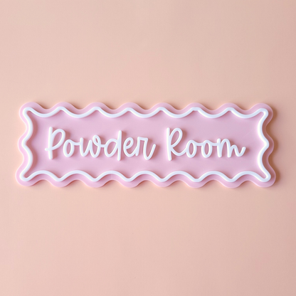 Pink acrylic Powder Room sign with white wavy border and script lettering on pastel background