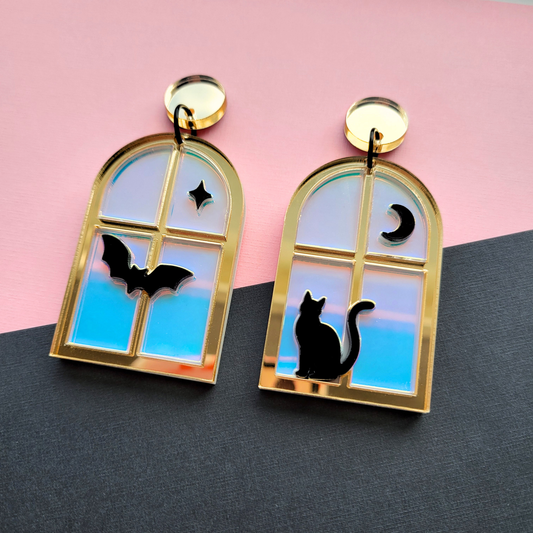 Gold acrylic window earrings with iridescent panes and black cat, bat, moon, and star silhouettes. Spooky cute handmade Halloween dangles.